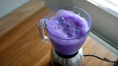 Mixer mit lila schaumigem Getränk auf Holztisch am Fenster in Küche